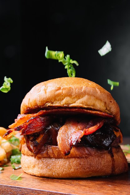 Primer plano vertical de una sabrosa hamburguesa con tocino sobre una pared negra