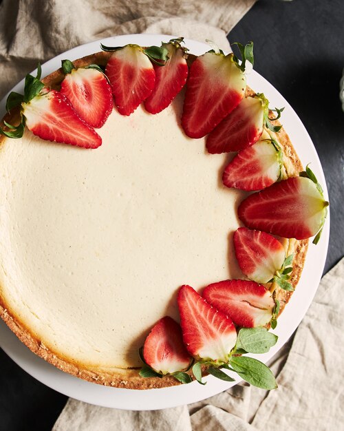 Primer plano vertical de una tarta de queso con fresa sobre una placa blanca.