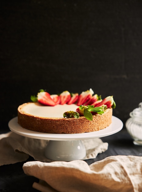 Primer plano vertical de una tarta de queso con fresa sobre una placa blanca.