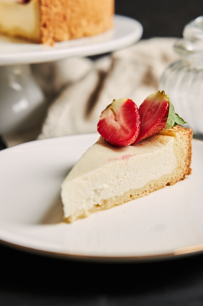 Primer plano vertical de una tarta de queso con fresa sobre una placa blanca.