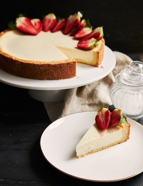 Primer plano vertical de una tarta de queso con fresa sobre una placa blanca.