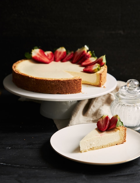 Primer plano vertical de tarta de queso de fresa sobre una placa blanca.