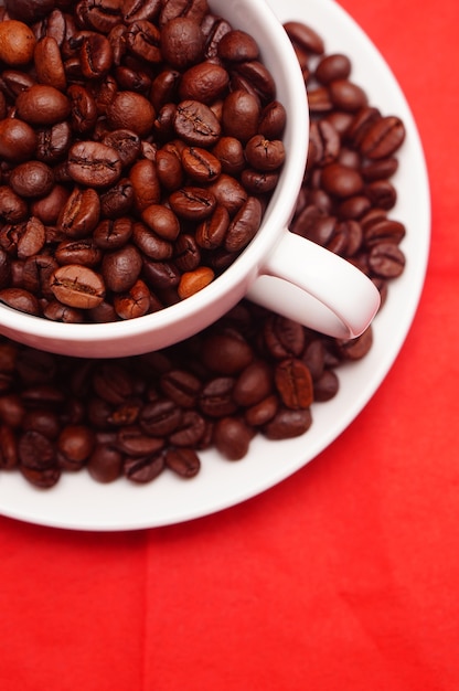 Primer plano vertical de una taza blanca llena de granos de café frescos en la mesa roja