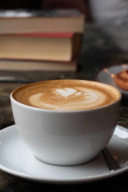 Primer plano vertical de una taza de café con leche cerca de algunos libros sobre una mesa