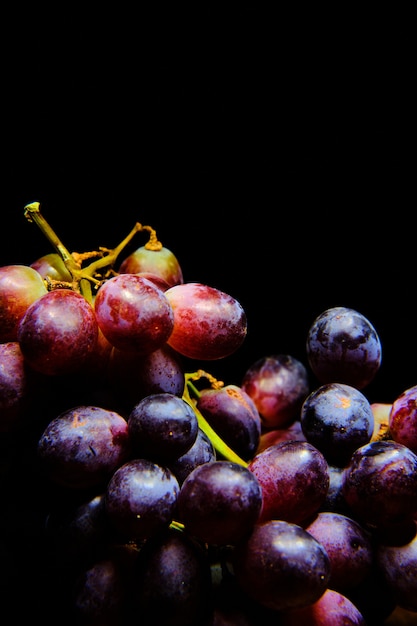Primer plano vertical de uvas rojas bajo las luces aislado sobre un fondo negro