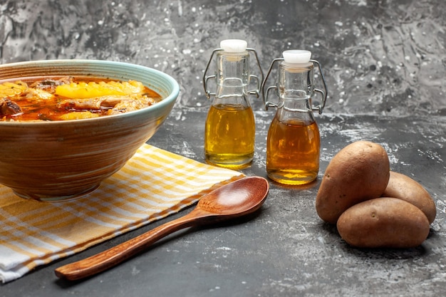 Foto gratuita primer plano y vista lateral de una deliciosa sopa con pollo y patatas y una cuchara en la mesa oscura y gris