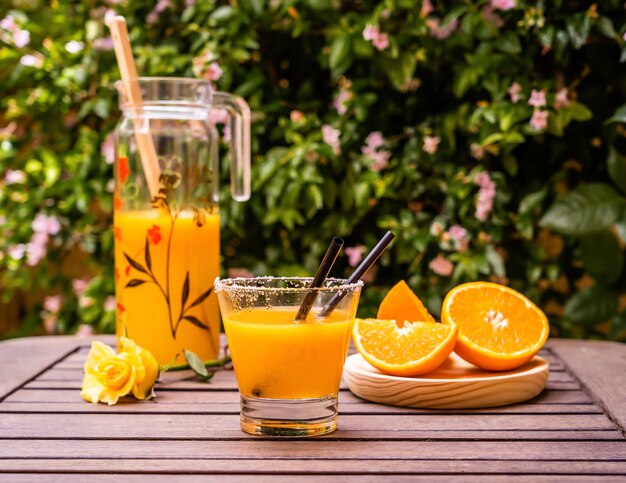 Primer plano de zumo de naranja natural con rodajas de naranja cortadas en una mesa de madera al aire libre