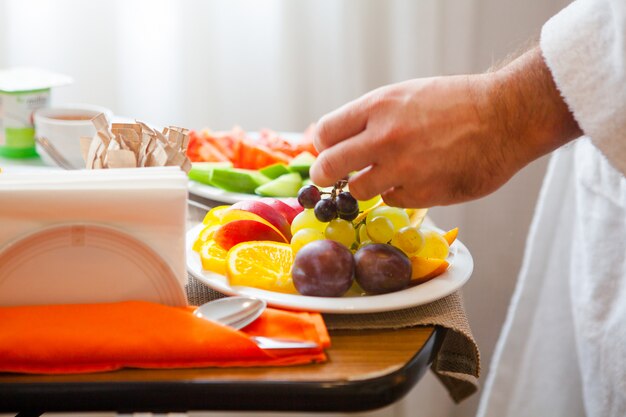 Primer plato de desayuno con frutas naranjas, manzana, uvas, ciruela, plato con tomate, pepino