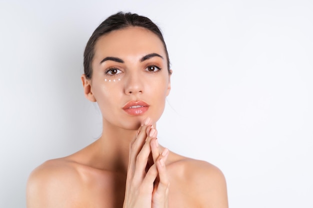 Primer retrato de belleza de una mujer en topless con piel perfecta y maquillaje natural con puntos de crema antienvejecimiento para hidratar y reafirmar la piel debajo de los ojosx9