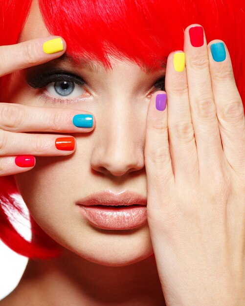 Primer rostro de una hermosa niña con uñas multicolores brillantes.
