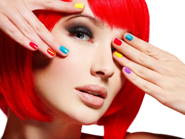 Primer rostro de una hermosa niña con uñas multicolores brillantes.