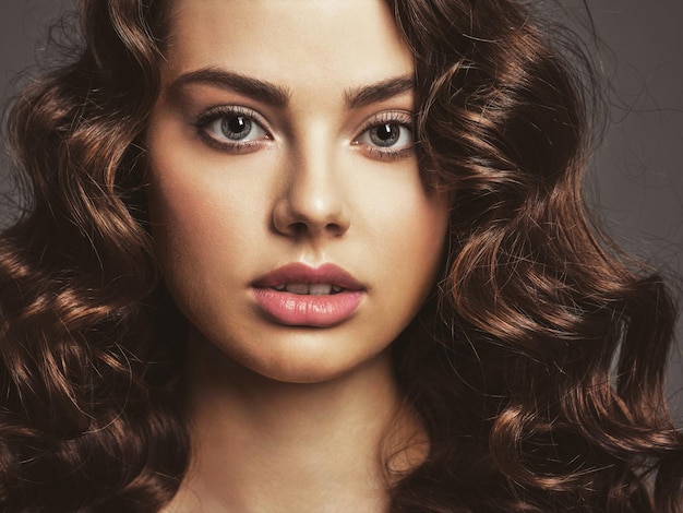 Primer rostro de una mujer hermosa con un maquillaje de ojos ahumado. Sexy y hermosa mujer de cabello castaño con cabello largo y rizado. Retrato de una atractiva mujer posando.