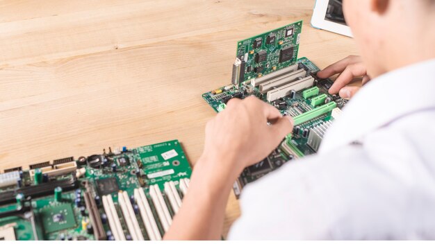 Primer del técnico de sexo masculino que repara la placa madre moderna de la PC en la tabla de madera