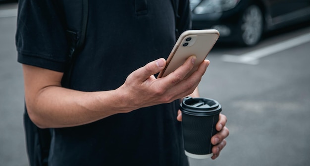Primer teléfono inteligente y un vaso de café en manos de un hombre