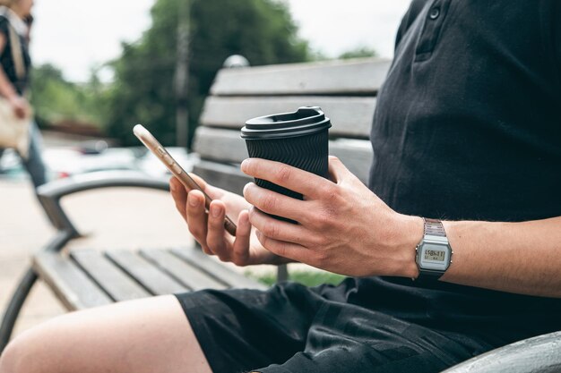 Primer teléfono inteligente y un vaso de café en manos de un hombre