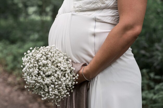 Primer tiro de una novia embarazada sosteniendo un ramo blanco en el día de su boda