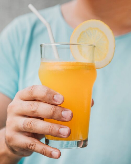 Primer vaso de jugo de naranja natural sostenido a mano