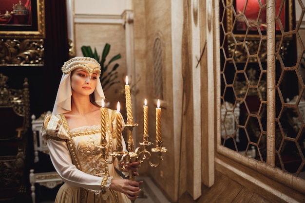 Princesa en ropa de oro lleva candelabro con velas encendidas