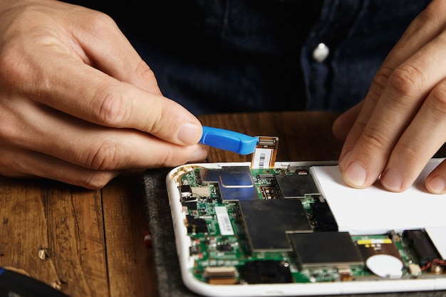 Pro utiliza un abridor de plástico especial para desenganchar el cable electrónico de la placa base en el servicio de reparación y reparación de dispositivos en el laboratorio