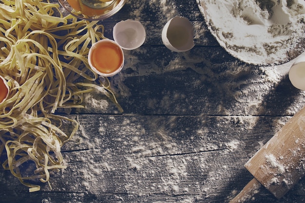 Proceso de cocinar la pasta con los ingredientes frescos crudos para la comida italiana clásica - huevos crudos, harina en la tabla de madera. Vista superior. Viraje.