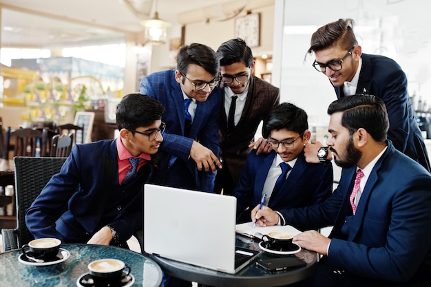 Proceso colaborativo de hombres de negocios indios durante una reunión de lluvia de ideas en la oficinaEquipo diverso de jóvenes vestidos con trajes que cooperan en el desarrollo de un proyecto común