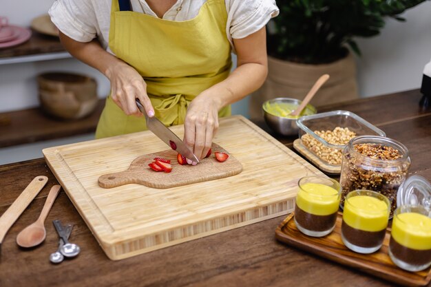 Proceso de elaboración del pudín de chía. Mujer corta fresa sobre tabla de madera.