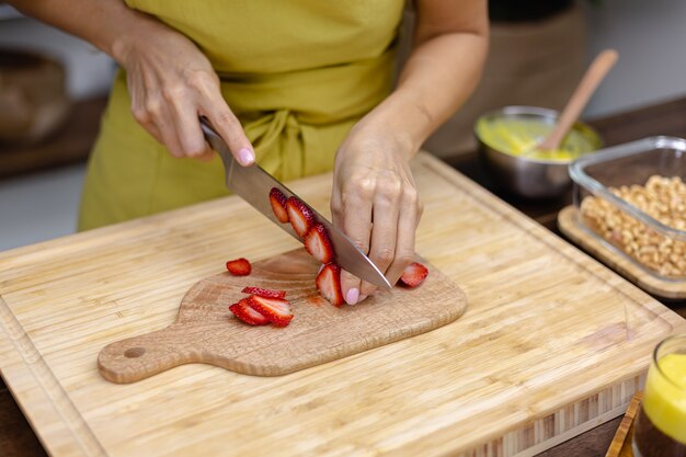 Proceso de elaboración del pudín de chía. Mujer corta fresa sobre tabla de madera.