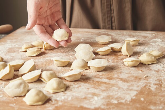 Proceso paso a paso de elaboración de albóndigas, ravioles o pelmeni caseros con relleno de carne picada utilizando molde para ravioles o máquina para ravioles. Listo para cocinar ravioles sobre tabla de madera, mano de mujer sostiene uno