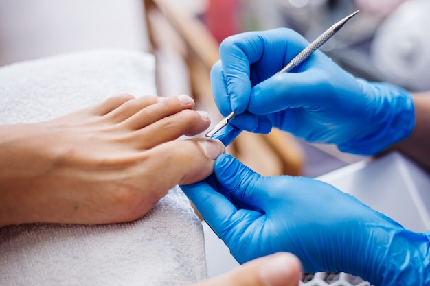 Proceso de pedicura Pedicura de salón en casa Tratamiento de cuidado de los pies y uñas El proceso de pedicura profesional Maestro en guantes azules hace pedicura