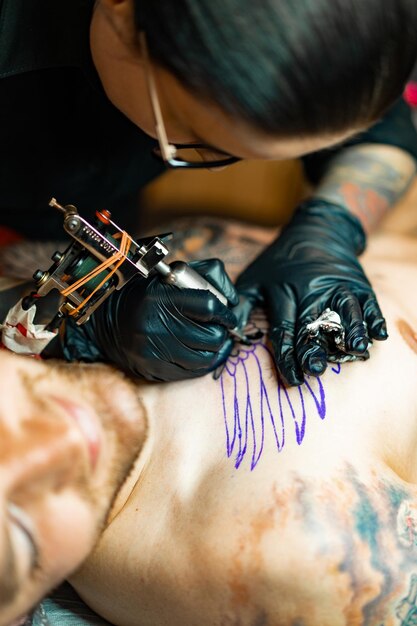 Proceso de salón de tatuajes. Una chica tatuadora rellenó un tatuaje. el proceso de rellenar un tatuaje en el cuerpo. Primer plano de las manos.