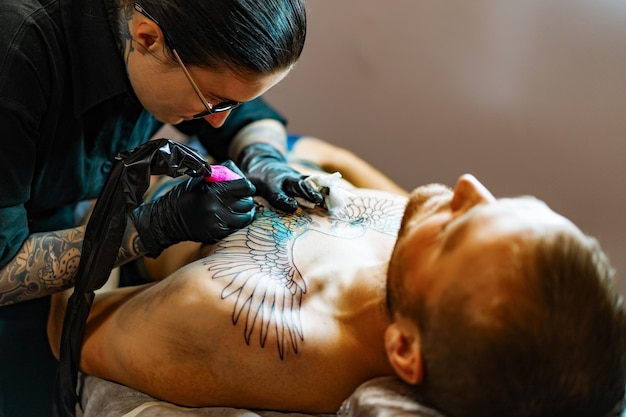 Proceso de salón de tatuajes. Una chica tatuadora rellenó un tatuaje. el proceso de rellenar un tatuaje en el cuerpo. Primer plano de las manos.