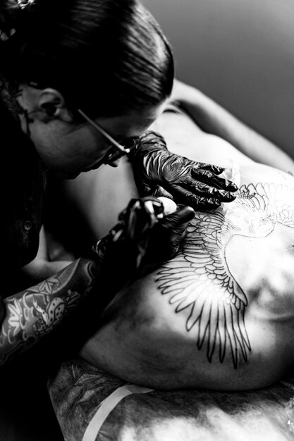 Proceso de salón de tatuajes. Una chica tatuadora rellenó un tatuaje. el proceso de rellenar un tatuaje en el cuerpo. Primer plano de las manos.