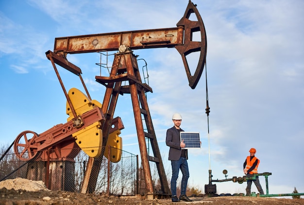 Proceso de trabajo de un gato de bomba e ingenieros en un campo petrolero en un día soleado