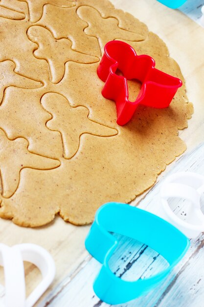 Proceso de tratar con las galletas de hombre de pan de jengibre, use molde de hombre de pan de jengibre rojo para cortar masa de pan de jengibre sobre papel de hornear alrededor de coloridos cortadores de galletas en la mesa de madera blanca. vista superior