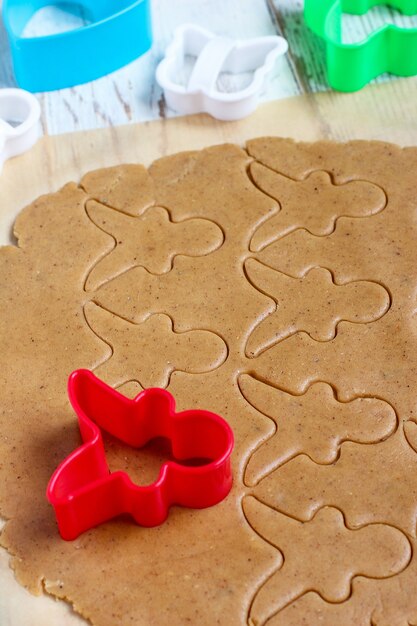 Proceso de tratar con las galletas de hombre de pan de jengibre, use molde de hombre de pan de jengibre rojo para cortar masa de pan de jengibre sobre papel de hornear alrededor de coloridos cortadores de galletas en la mesa de madera blanca. vista superior