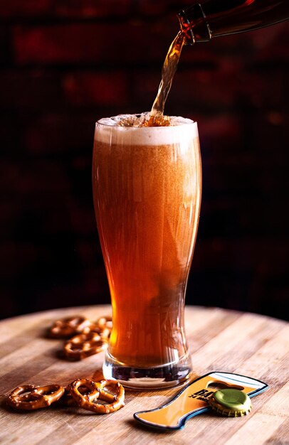 Proceso de verter cerveza ámbar en el vaso sobre una tabla de madera y bocadillos