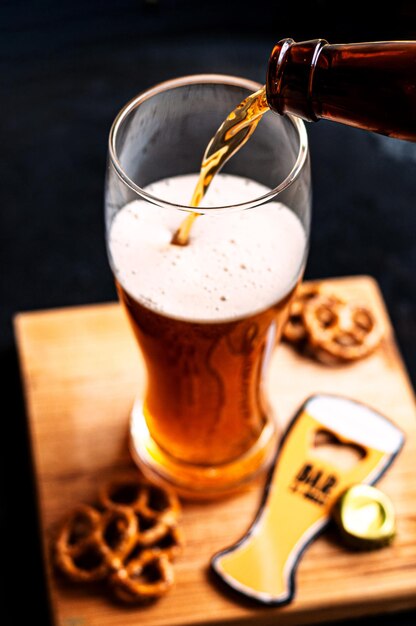 Proceso de verter cerveza ámbar en el vaso sobre una tabla de madera y bocadillos