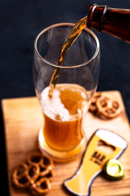 Proceso de verter cerveza ámbar en el vaso sobre una tabla de madera y bocadillos