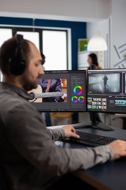 Producción de video gráfico trabajando en una PC con dos pantallas que editan imágenes de video y audio en un lugar de trabajo creativo