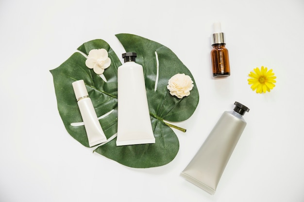 Producto cosmético y flor en monstera hoja y botella de aceite esencial sobre fondo blanco