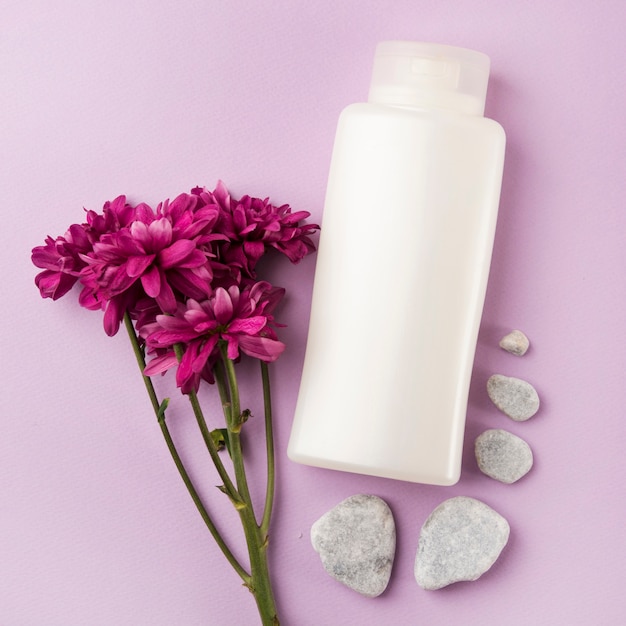 Producto de cosméticos blanco con flores rosas y piedras de spa sobre fondo rosa