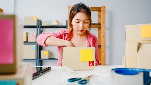 Producto de embalaje de empresaria joven empresaria de Asia en caja de cartón entregar al cliente, trabajando en la oficina en casa. Propietario de una pequeña empresa, puesta en marcha de la entrega del mercado en línea, concepto independiente de estilo de vida.