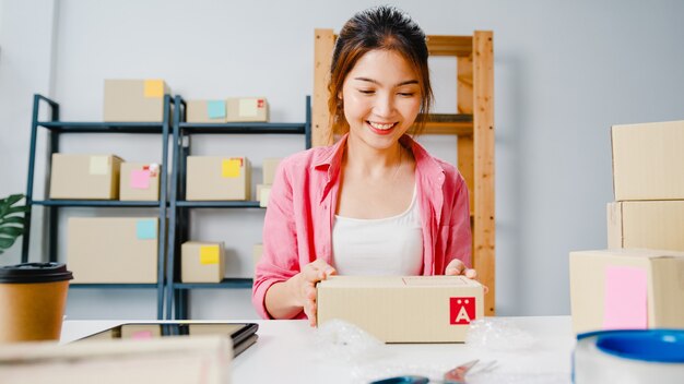 Producto de embalaje de empresaria joven empresaria de Asia en caja de cartón entregar al cliente, trabajando en la oficina en casa. Propietario de una pequeña empresa, puesta en marcha de la entrega del mercado en línea, concepto independiente de estilo de vida.