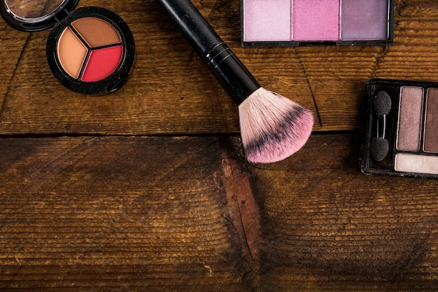 Productos cosméticos con pincel de maquillaje sobre fondo de madera