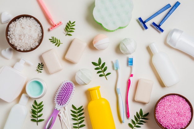 Productos cosméticos con sal; cepillo de dientes; maquinilla de afeitar; cepillo para el pelo y hojas sobre fondo blanco