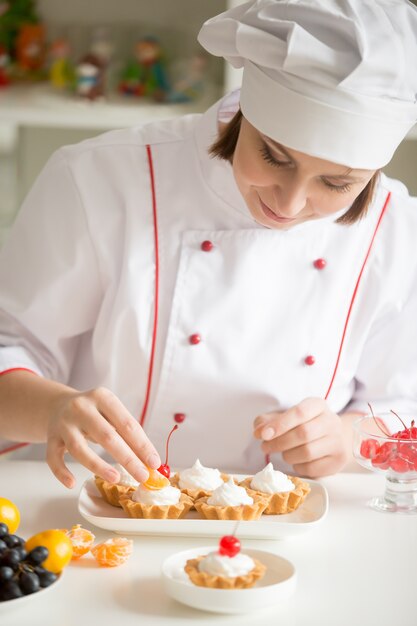 Profesional confitero femenina decorar mini tarta de frutas