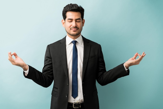 Profesional masculino en traje gesticulando mientras medita sobre fondo azul