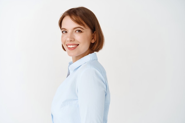 Profesional de negocios. Retrato de mujer joven confiada en blusa de oficina, gira la cabeza y sonriendo seguro de sí mismo, de pie sobre la pared blanca