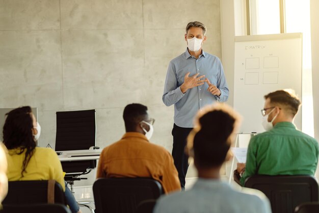 Profesor adulto medio con mascarillas protectoras hablando con un grupo de estudiantes universitarios en una sala de conferencias