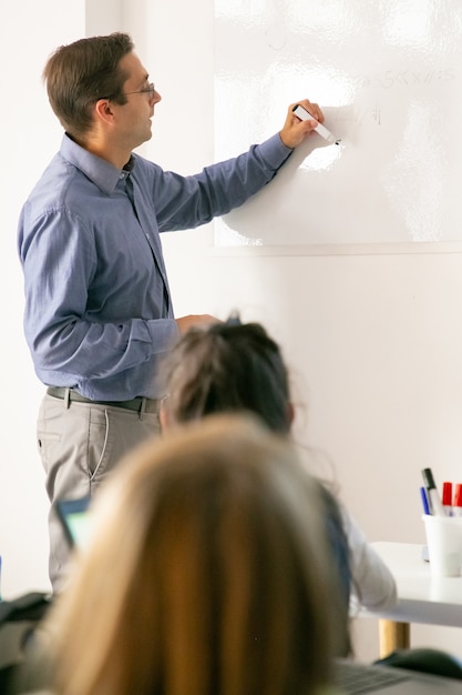 Foto gratuita profesor concentrado dibujando a bordo y explicando la lección a los alumnos